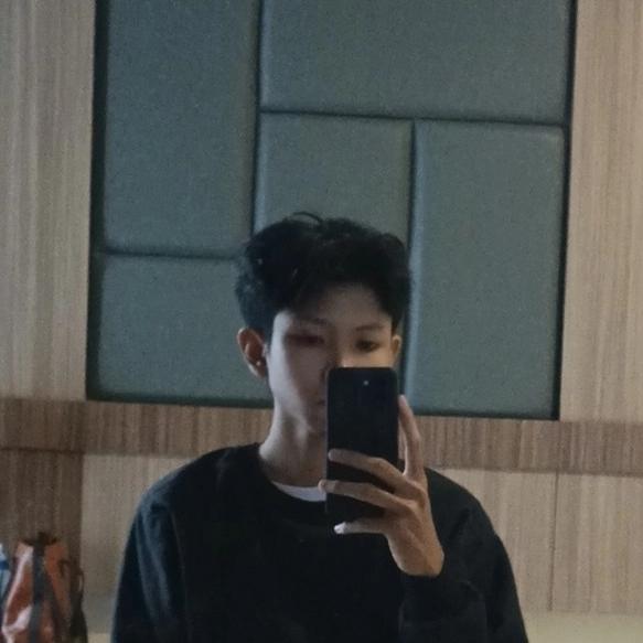 A handsome man holding a phone in front of a mirror with a black jacket and messy hair